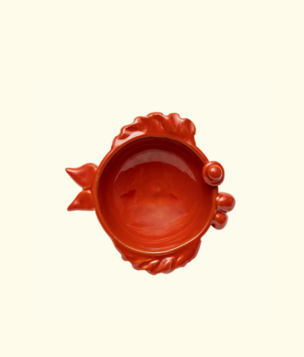 Red ceramic bowl with decorative handles on a beige background